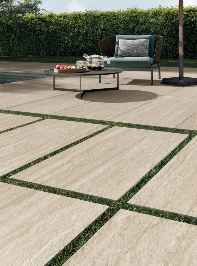 Perpetual di Panaria Ceramica interpreta travertino e marmo in un gres ad alta resistenza. Qui nella finitura Travertino Cream da 20 mm, posata a secco sull’erba